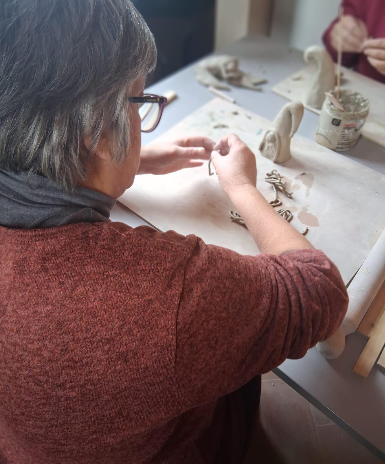 img title Donna con giacca prugna lavora su un piccolo diorama con muschio e figure, durante un laboratorio creativo del centro diurno.