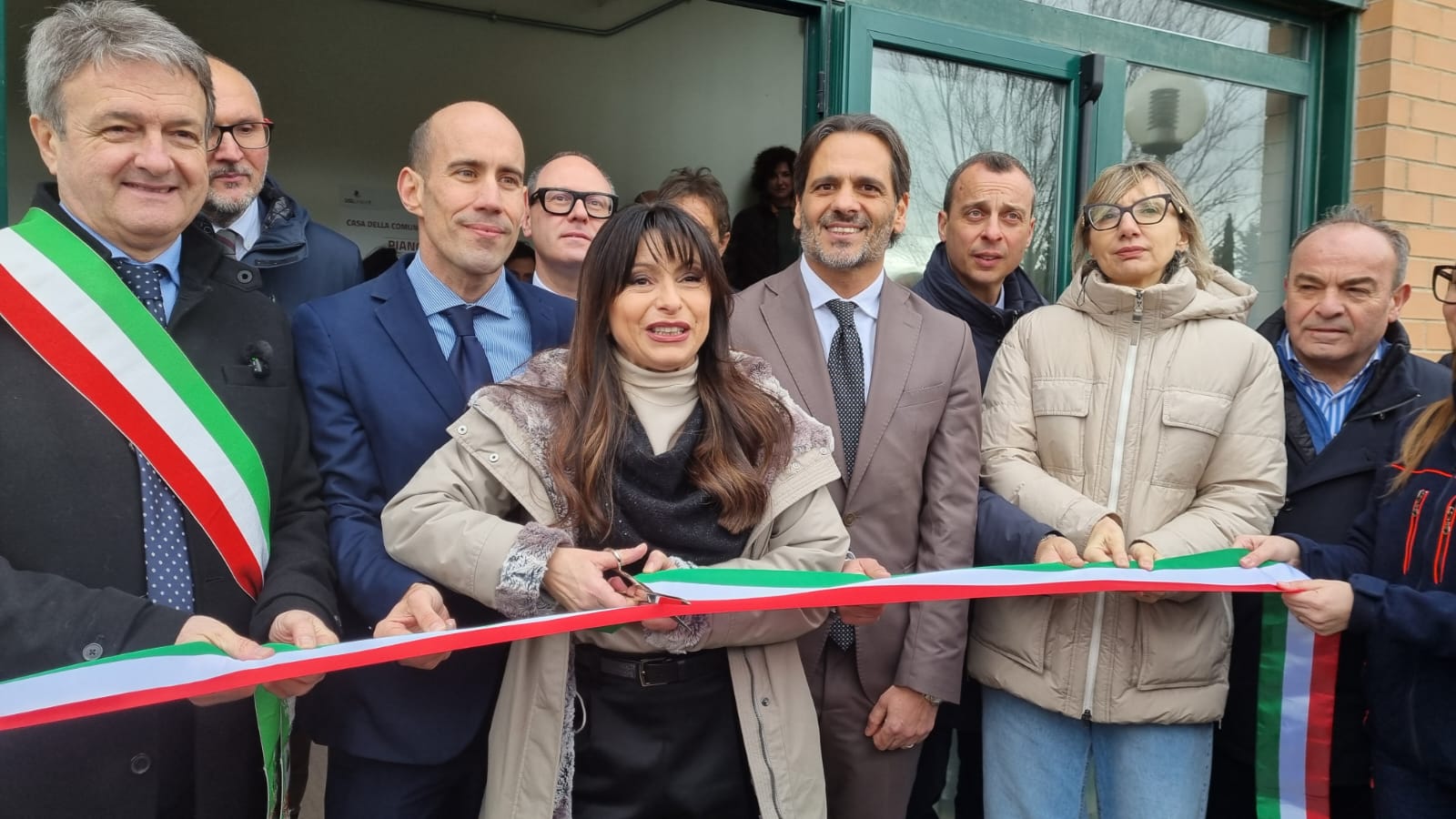 La presidente della Regione Umbria Stefania Proietti taglia il nastro tricolore all'ingresso della nuova Casa della Comunità di Magione, circondata dalle autorità locali.