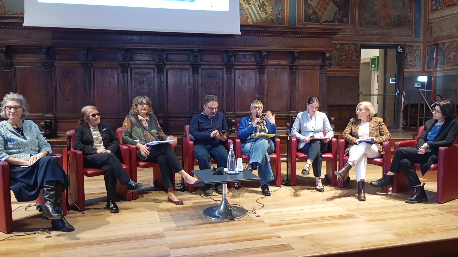 img title Tavola rotonda con otto relatrici e relatori seduti in poltrone rosse sul palco della Sala dei Notari.