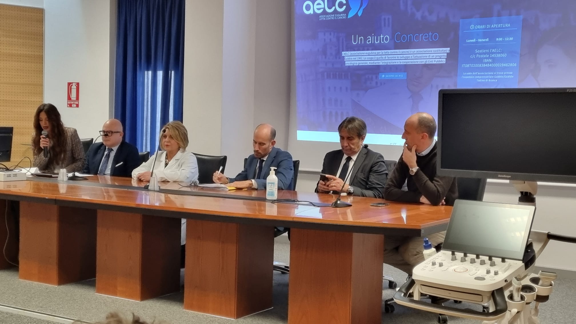 img title Relatori istituzionali seduti al tavolo durante la cerimonia di donazione con l'ecografo Sonoscape P25 Elite in primo piano a destra.