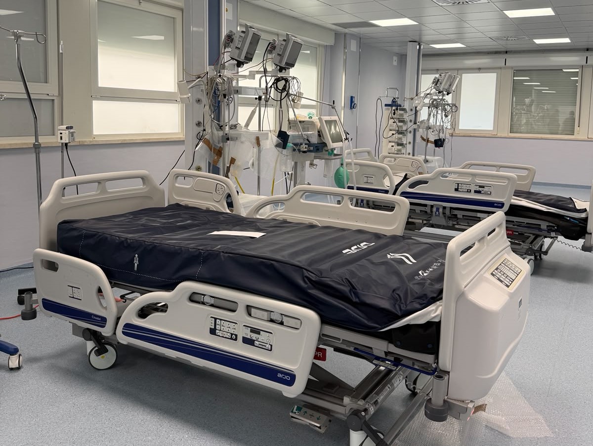 img title Panoramica della nuova area degenza open space di terapia intensiva, dotata di moderni letti ospedalieri articolati con materassi blu antipiaghe, stativi per flebo e pensili tecnici attrezzati con monitor e pompe infusionali.