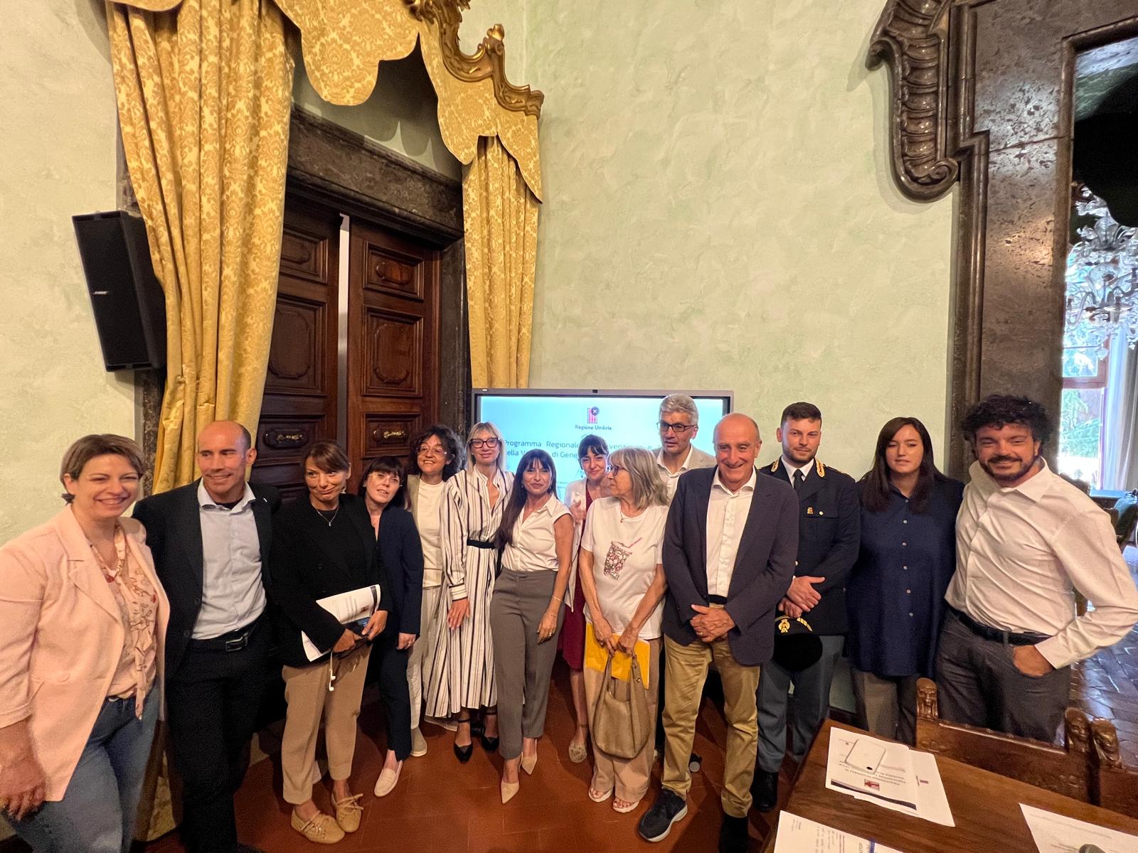 img title Foto di gruppo con numerosi rappresentanti istituzionali in posa in una sala affrescata, davanti a un monitor che mostra il titolo di un evento regionale.