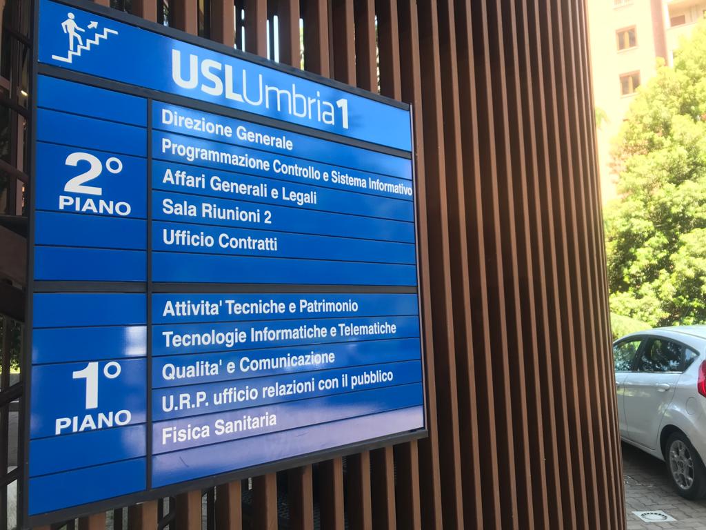Targa segnaletica blu con logo USL Umbria 1 contenente l'indicazione dei servizi e degli uffici del primo e secondo piano.