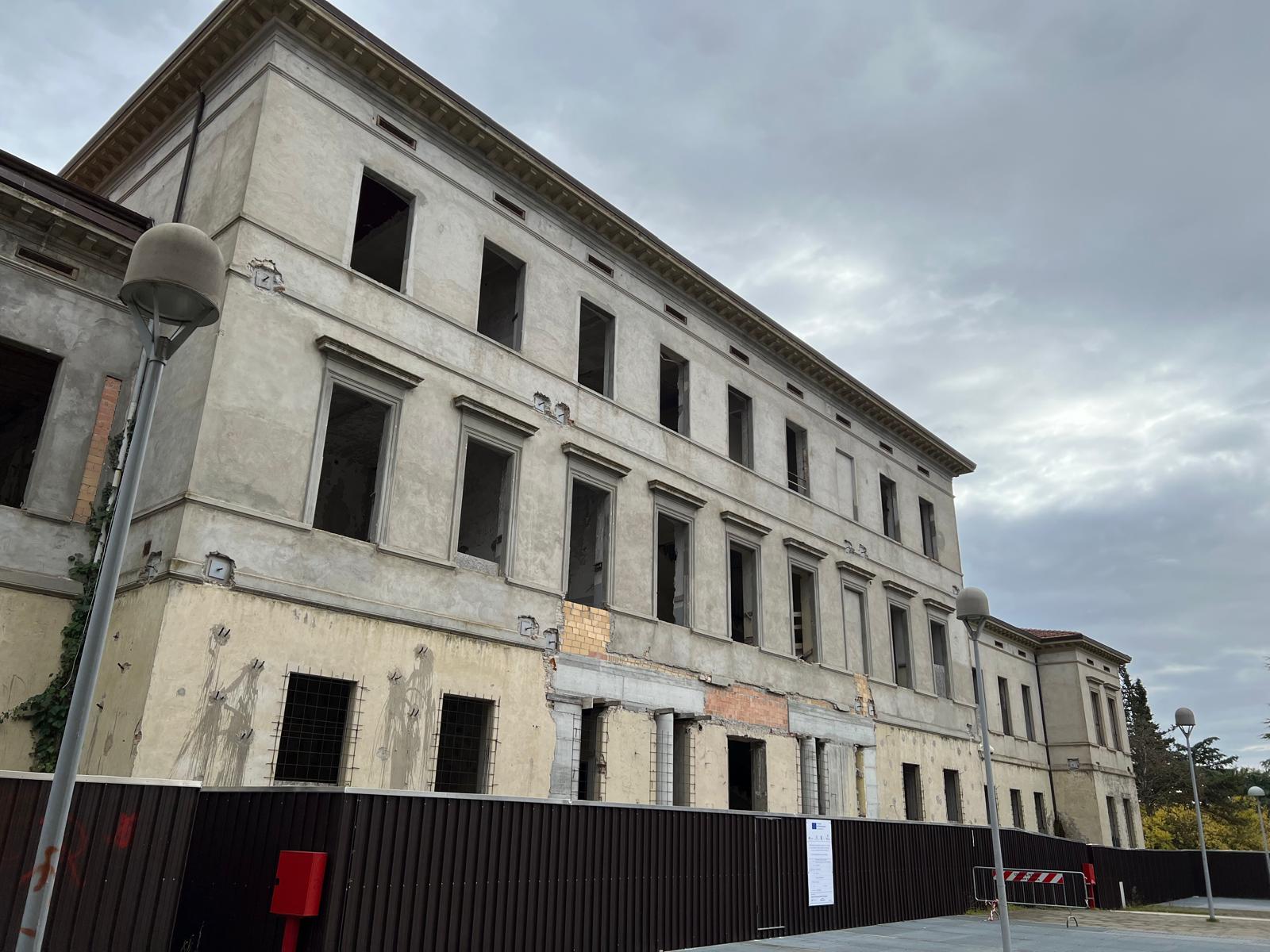 img title Edificio storico in ristrutturazione destinato alla nuova Casa della Comunità di Perugia, circondato da recinzioni di cantiere.